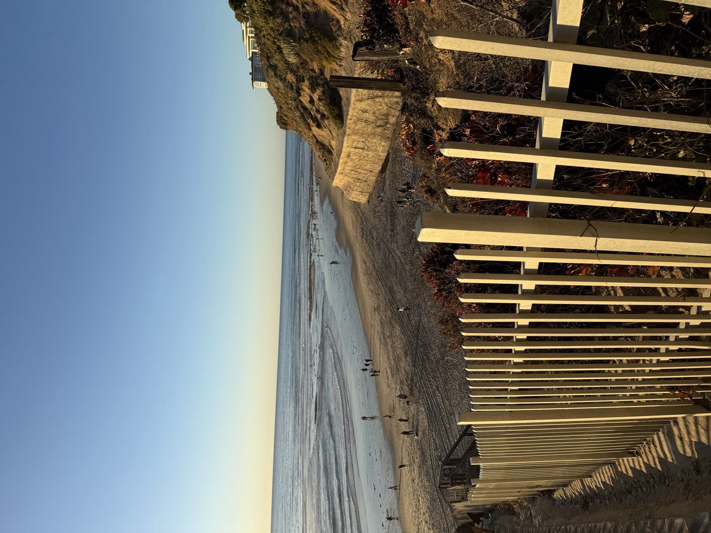 Beach access stairs and fence in late light, crowds on the sand below the bluffs